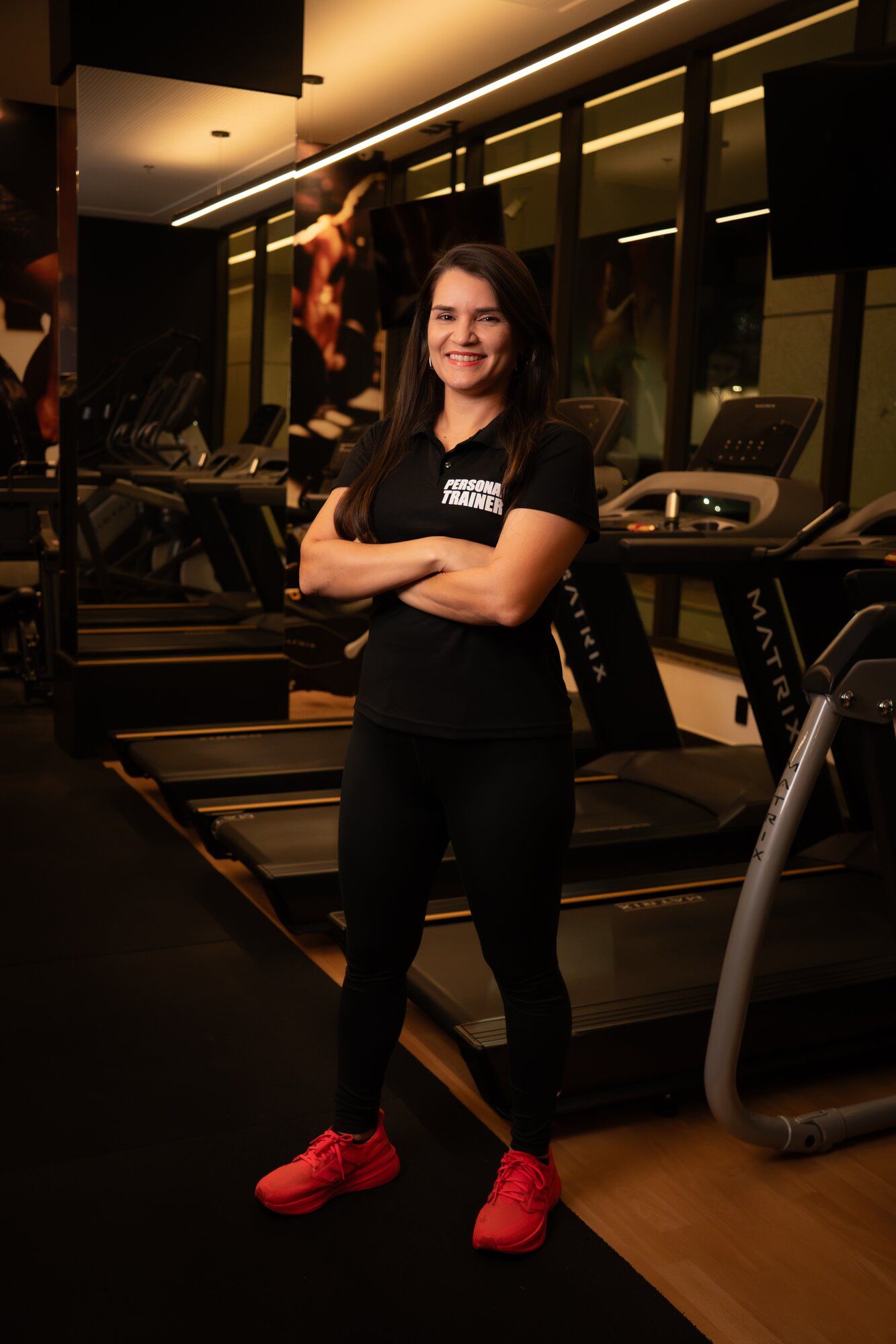 Licia Furtado, personal trainer presencial, de braços cruzados na academia em Brasília